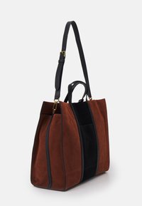 Grand tote en daim brun et noir, présentant un design structuré, des poignées supérieures doubles et une bandoulière en cuir noir réglable.