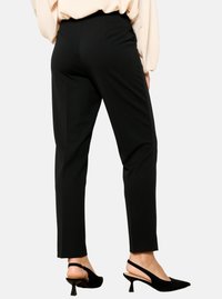 Črne zožene hlače iz gladkega, raztegljivega materiala z srednjim pasom; oblečene z črnimi slingback petami za eleganten videz.