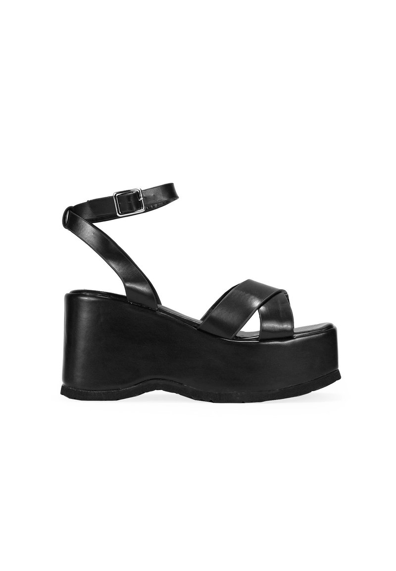 Sandalias de plataforma negras con una suela de cuña gruesa, diseño de correas cruzadas y correa de tobillo ajustable en material de cuero suave.