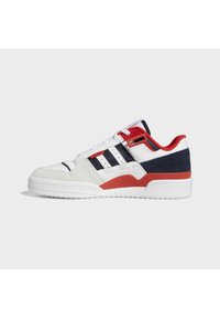 Baskets basses blanches avec des bandes noires, des accents rouges et une semelle blanche épaisse, vues de côté sur un fond gris clair.