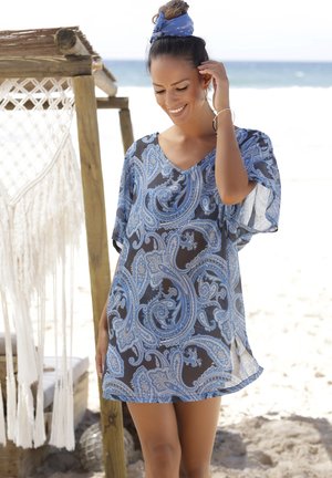 Abito coprente a stampa paisley blu realizzato in tessuto leggero, con scollatura a V, maniche corte e vestibilità ampia, ambientato su uno sfondo da spiaggia.