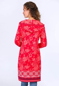 Roter Blumenmuster langer Kapuzenpullover mit Kapuze, mit einem blauen Spitzenabschluss und einem weichen, strukturierten Stoff. Kombiniert mit enganliegenden Jeans.