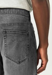 Hallid teksased, millel on tagaküljel diskreetne õmblusdisain, kõrge vöökoht ja tekstuuriga kangas.