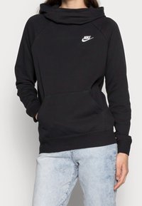 Svart Nike-huvtröja med hög, vikbar krage, ficka fram och ribbade ärmslut; har en vit logotyp på vänster bröstområde.