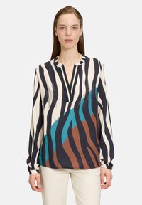 Blouse à manches longues en crème avec des rayures noires et bleues, dotée d'une patte de boutonnage partielle et d'une coupe décontractée. Impressions texturées en marron.