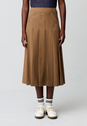 Falda midi plisada marrón con botones decorativos, usada con calcetines blancos con rayas verdes y zapatos blancos con cordones.