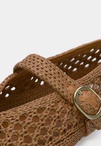 Sandale tissée marron clair avec un design perforé, dotée d'une large bride et d'une boucle circulaire dorée en accent.