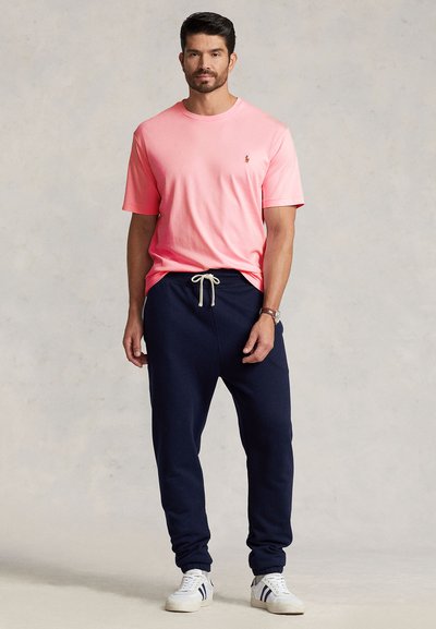 Różowy bawełniany T-shirt z małym logo, do tego granatowe spodnie dresowe z elastycznym pasem i białym sznurkiem, uzupełnione białymi trampkami.