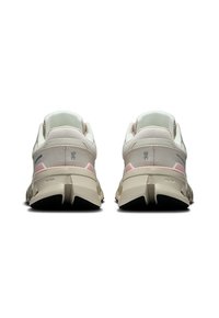 Een paar beige en roze sportschoenen weergegeven vanuit de achterkant met dikke zolen en zichtbare merknummers op de hielen.