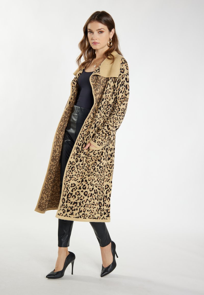 Leoprint langer Cardigan in Beige und Schwarz, mit einem einfarbigen beigen Kragen. Getragen über einem schwarzen Top und Lederhosen, mit schwarzen hohen Schuhen.