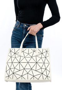 Biała torba tote o geometrycznym kształcie z czarnym trójkątnym wzorem, wykonana z gładkiego materiału syntetycznego, z wytrzymałymi uchwytami, prostokątna forma i zapięciem na zamek.