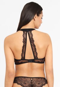 Černý krajkový bralet s designem na halter; obsahuje jemné krajkové detaily na zádech a nastavitelné zapínání pro dokonalé padnutí.