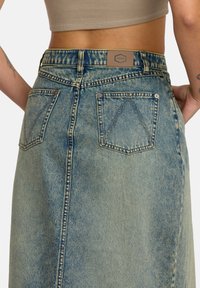 Jeanskjørt med en falmet lys blå vask, med middels høyde midje, to baklommer og et lærmerke på linningen.