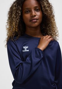 Mörkblå långärmad skjorta i slätt tyg med en vit logotyp på vänster bröst. Slim fit med rund halsringning och elastiska muddar.