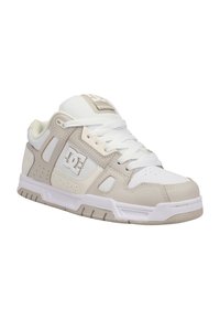 Beige og hvit sneaker med overdel i skinn og mesh, perforerte detaljer, polstret krage og gummisåle. DC-logo på siden.