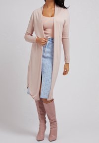 Dlouhý světle růžový kardigan přes přiléhavý růžový top a modrou džínovou sukni s květinovými vzory. Outfit doplňují růžové vysoké boty z měkkého materiálu.