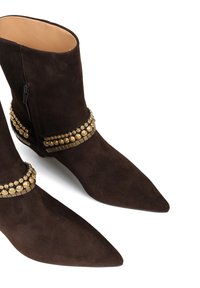 Brązowe zamszowe botki za kostkę z ostrymi noskami, ozdobione dekoracyjnymi złotymi elementami wokół kostki i bocznym zamkiem błyskawicznym.