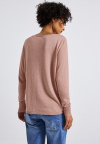 Helles rosa Sweatshirt mit langen Ärmeln, gerippten Bündchen und entspannter Passform, kombiniert mit blauen Jeans. Der Stoff wirkt weich mit feiner Textur.