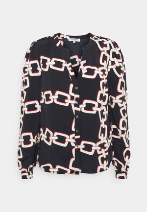 Blouse noire à manches longues avec motif chaîne blanche et rouge, boutonnée sur le devant, avec épaules légèrement bouffantes.