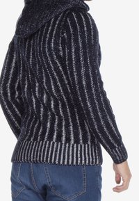 Sweter z dzianiny z kapturem, w pionowe granatowe i srebrne paski. Ściągacze na mankietach i u dołu oraz fakturowana tkanina dla zapewnienia ciepła.