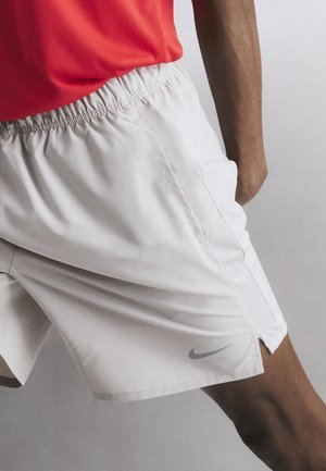 Osoba u bijelim Nike sportskim hlačicama i crvenoj majici, u dinamičnom položaju na jednobojnoj pozadini.