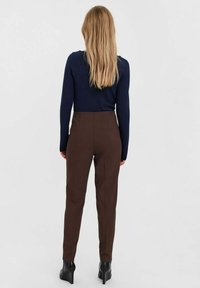 Braune, maßgeschneiderte Hose mit hoher Taille, glatter Textur und geradem Bein, kombiniert mit einem navyblauen Langarmoberteil. Schwarze, hochhackige Schuhe.