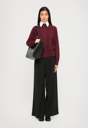 Naine kannab burgundi värvi lukuga sviitri, millel on valge krae, laiad mustad püksid, musti kingi ning tal on õlal suur must tekstuuriga käekott.