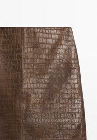 Jupe en simili cuir marron avec un motif texturé de peau de crocodile, présentant une finition lisse et une silhouette ajustée.
