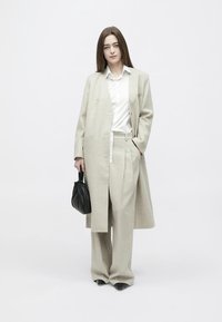 Palton și pantaloni gri deschis, croiți, cu o cămașă albă dedesubt. Geantă neagră cu design adunat. Textură netedă, croială lejeră.