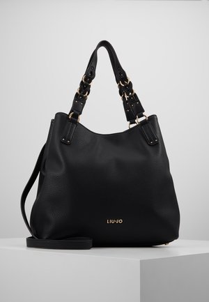 Czarna torebka ze skóry o fakturze, z podwójnymi plecionymi uchwytami, długim paskiem i złotym logo "LIU JO" na przedzie, prezentowana na białym piedestale.