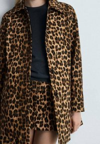 Leopardikuosis takki, joka on valmistettu pehmeästä kankaasta, jossa on jämäkkä muotoilu. Takissa on napitus, leveä kaulus ja siihen sopiva leopardikuosis hame.