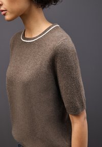 Maglione in maglia marrone con maniche corte, caratterizzato da un colletto a coste bianco e una texture morbida, che mostra una vestibilità rilassata e dettagli di design minimal.