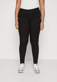 Sorte tettsittende jeans med en glatt tekstur, som har knapplås og glidelås, frontlommer og en tettsittende design. Kombinert med hvite sneakers.