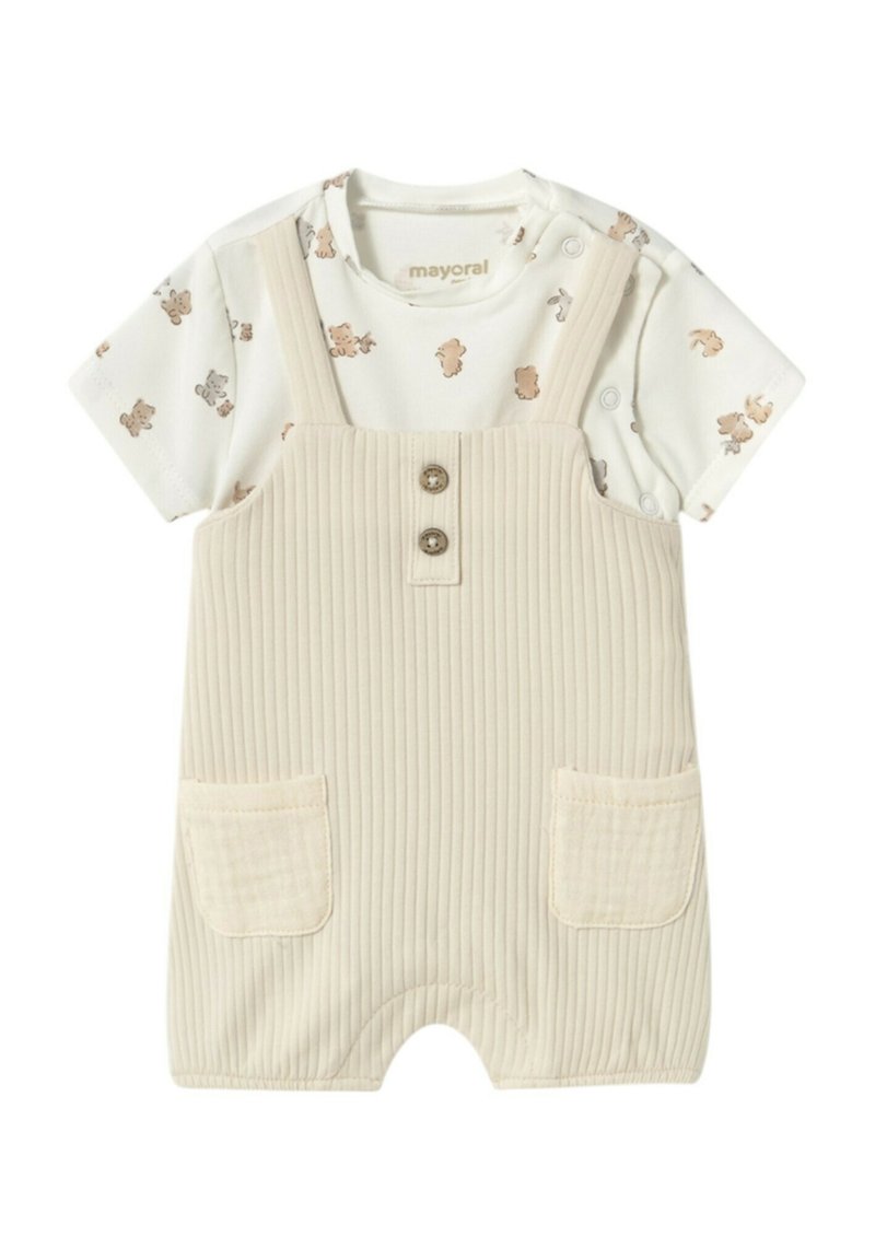 Peto de color beige con relieve, con dos bolsillos y cierre de botones. Debajo lleva una camiseta blanca con un estampado de animales marrones.