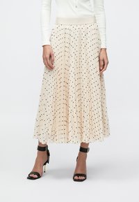 Plissé midi-rok in lichtbeige met zwarte polka dots, voorzien van een elastische tailleband en zachte, textuurrijke stof.