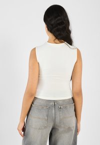 Weißes ärmelloses Oberteil mit tailliertem Design, kombiniert mit hoch geschnittenen hellgrauen Jeans aus Denim, die zwei Gesäßtaschen und sichtbare Nähte aufweisen.