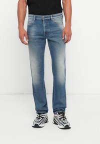 Vaqueros rectos de mezclilla de color azul claro, con un ligero desgaste, cinco bolsillos y cierre de botón, combinados con zapatillas deportivas negras.