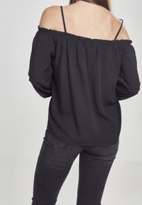 Mustatuista olkapään päältä oleva pusero, jossa on joustava kaula-aukko, pitkät hihat ja kevyt kangas, yhdistettynä tummiin farkkuihin. Yksinkertainen ja vartalonmyötäinen muotoilu.