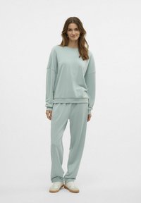 Lyseblå, oversized sweatshirt med dropped shoulders og matchende lette joggers. Fremstillet af blødt stof, parret med hvide sneakers.