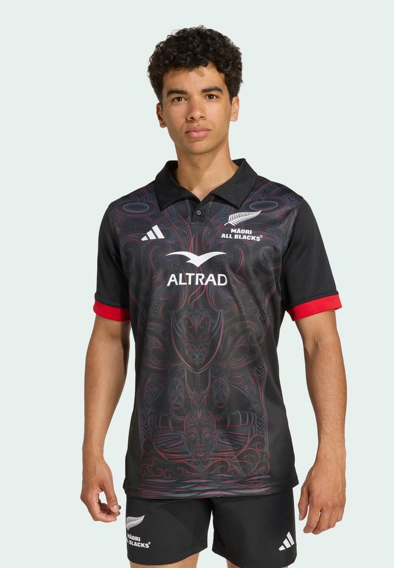 Sort rugby polo shirt med røde accenter, der har intrikate røde mønstre. Logo på brystet og producentens branding på højre ærme.