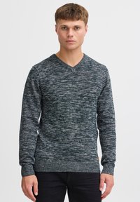 Mørkegrønn strikket genser med V-hals, lange ermer og en teksturert overflate. Har ribbede kanter og mansjetter med et lite merket lapp.