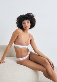 Bralet în roz deschis de la Calvin Klein, împreună cu chiloți asortați, au benzi cu logo alb. Materialul este neted, cu un design minimalist și bretele subțiri.