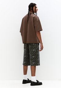 Brown oversized t-shirt with short sleeves, paired with knee-length gray shorts featuring a dark leopard print. Black shoes and white socks.