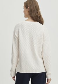 Pull en crème texturé avec une coupe ample, des poignets et un ourlet côtelés, présentant un motif en nid d'abeille et un grand col rond.