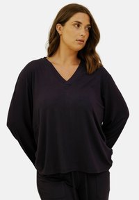 Haut noir à encolure en V, coupe ample, fabriqué en tissu doux. Manches longues et silhouette décontractée. Design minimaliste sans motifs ni accents.