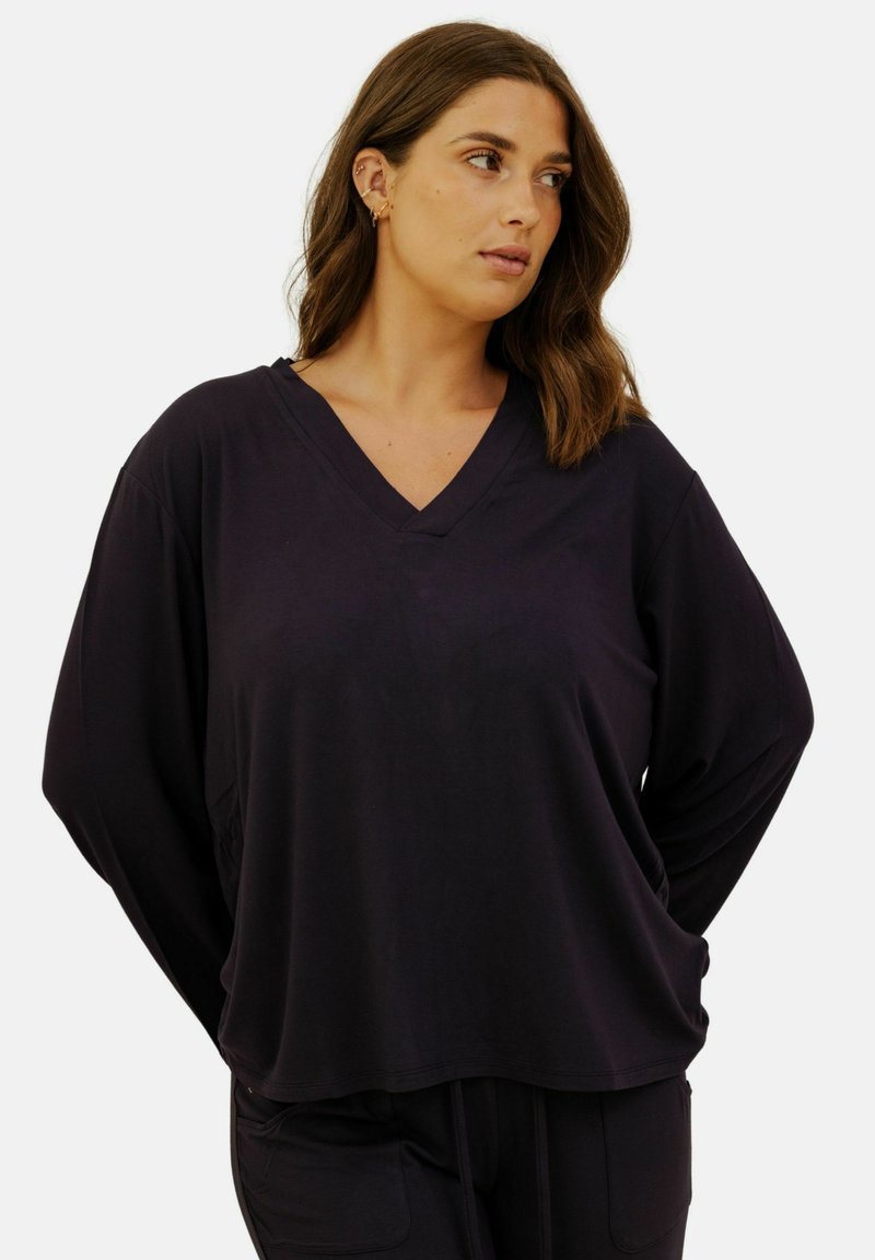 Haut noir à encolure en V, coupe ample, fabriqué en tissu doux. Manches longues et silhouette décontractée. Design minimaliste sans motifs ni accents.