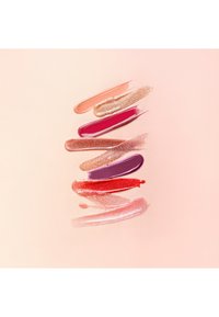 Swatches of glossy and shimmery lip color in peach, gold, magenta, bronze, purple, red, and pink shades on pale peach background.