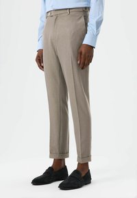 Beige, maßgeschneiderte Hose mit glatter Textur, ausgestattet mit einem einzelnen Knopfverschluss und aufgerollten Beinabschlüssen, kombiniert mit schwarzen Wildlederloafern.