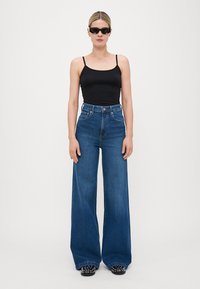 Svart tank top i kombination med högmidjade, vida blå denimjeans. Accenterad med svarta skor med vita prickar.