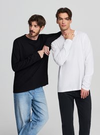 Czarno-białe długie koszulki z okrągłymi dekoltami, połączone z niebieskimi i czarnymi dżinsami, prezentowane na dwóch modelach.